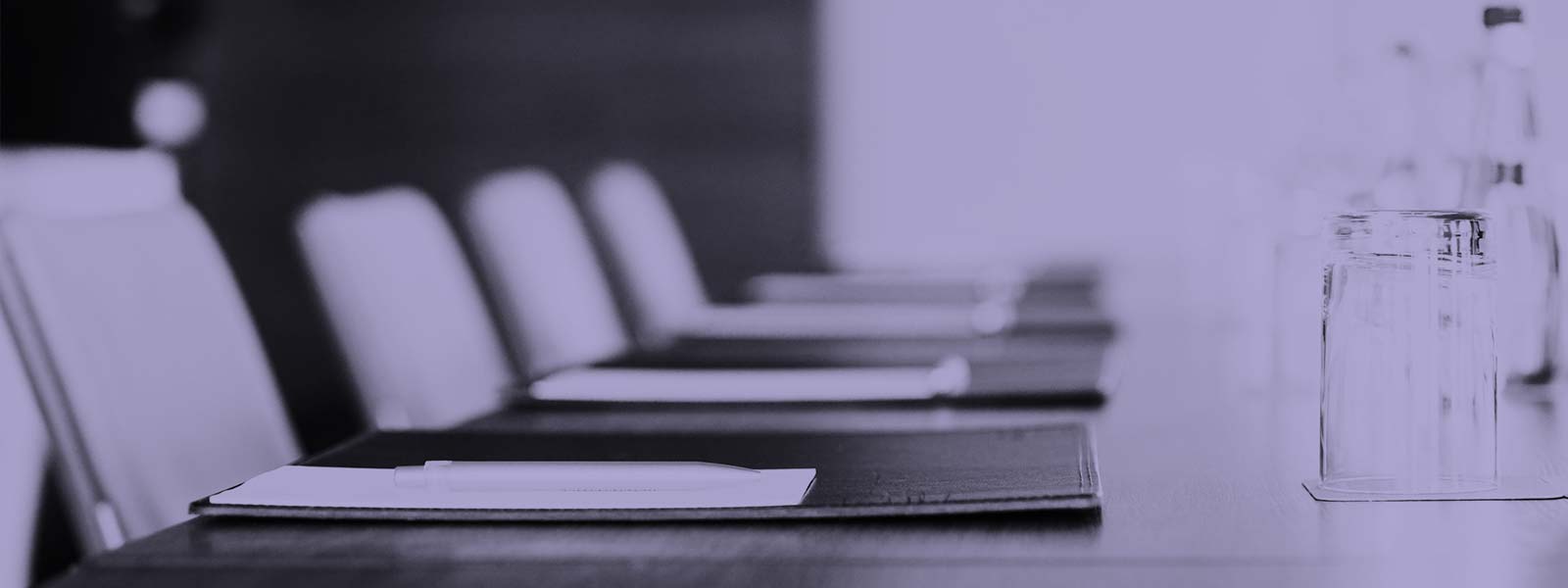 Side view of a meeting room desk, with four chairs, pads, pens, and glasses of water.