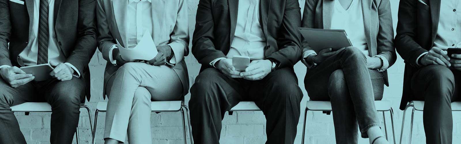A row of people in suits sitting on a row of chairs