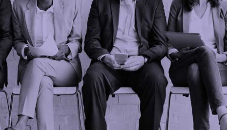 A row of four sitting on chairs with their faces concealed. They are all wearing business dress.