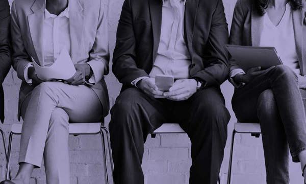 A row of four sitting on chairs with their faces concealed. They are all wearing business dress.