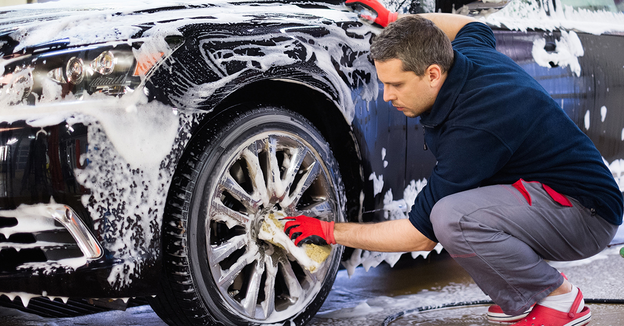 A man washing a car's front wheel