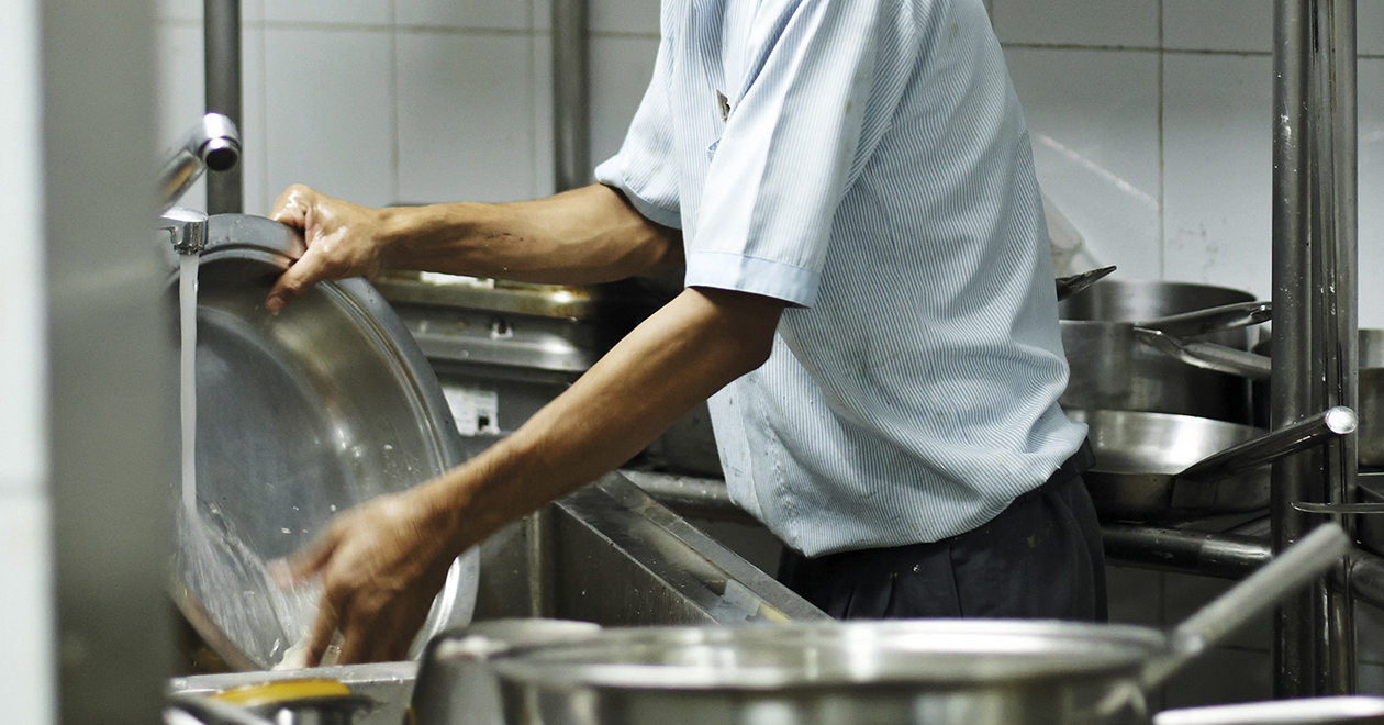 A person washing up in an industrial kitchen