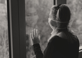A woman wearing a face mask looking out of a window