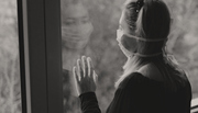 A woman wearing a face mask looking out of a window