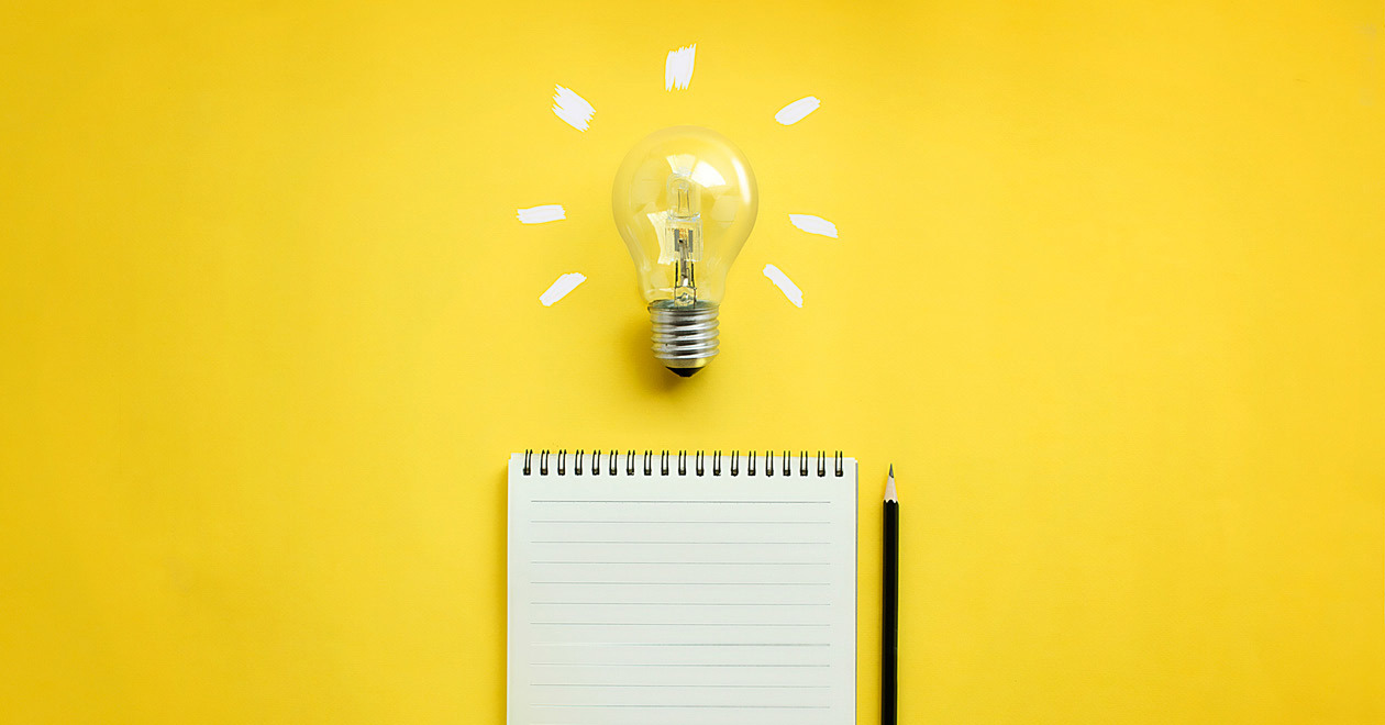 Light bulb above note pad on yellow background