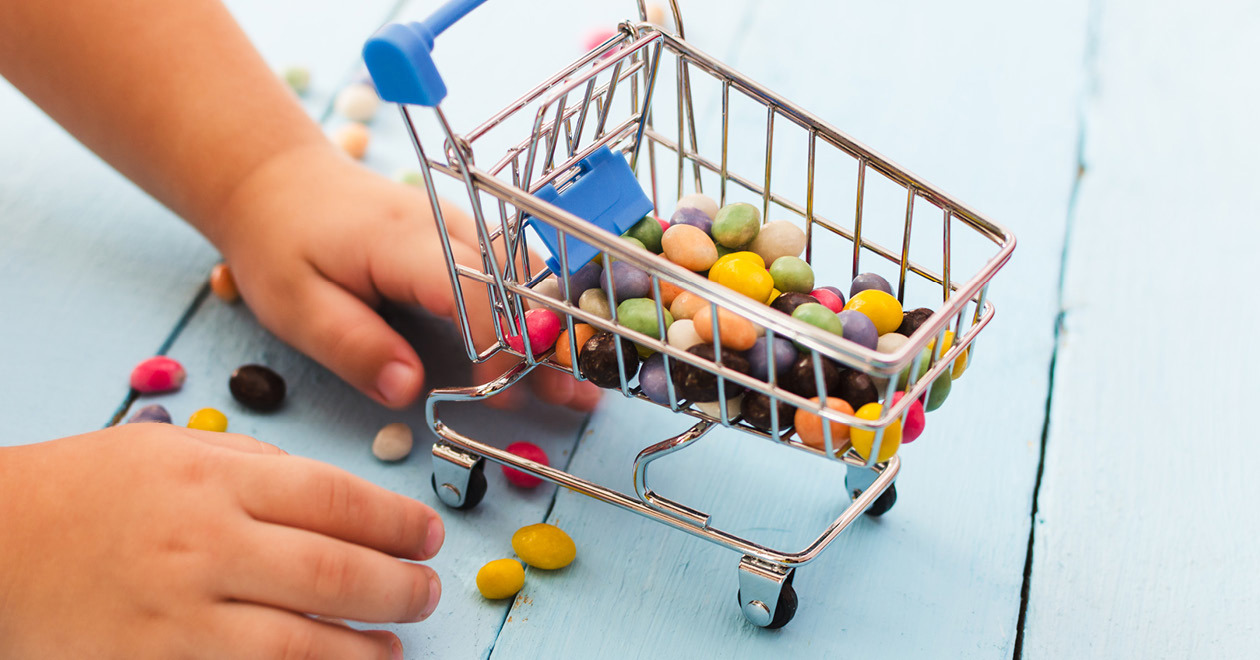 Child's hands collecting loose candy into a mini trolley