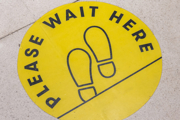 'Wait here' sign on the floor of a shop.
