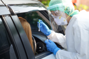 A medical professional carrying out a COVID-19 test on the driver of a car, through the car window.