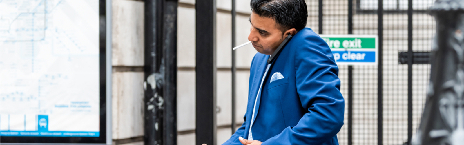 A man cradles a mobile phone while smoking a cigarette
