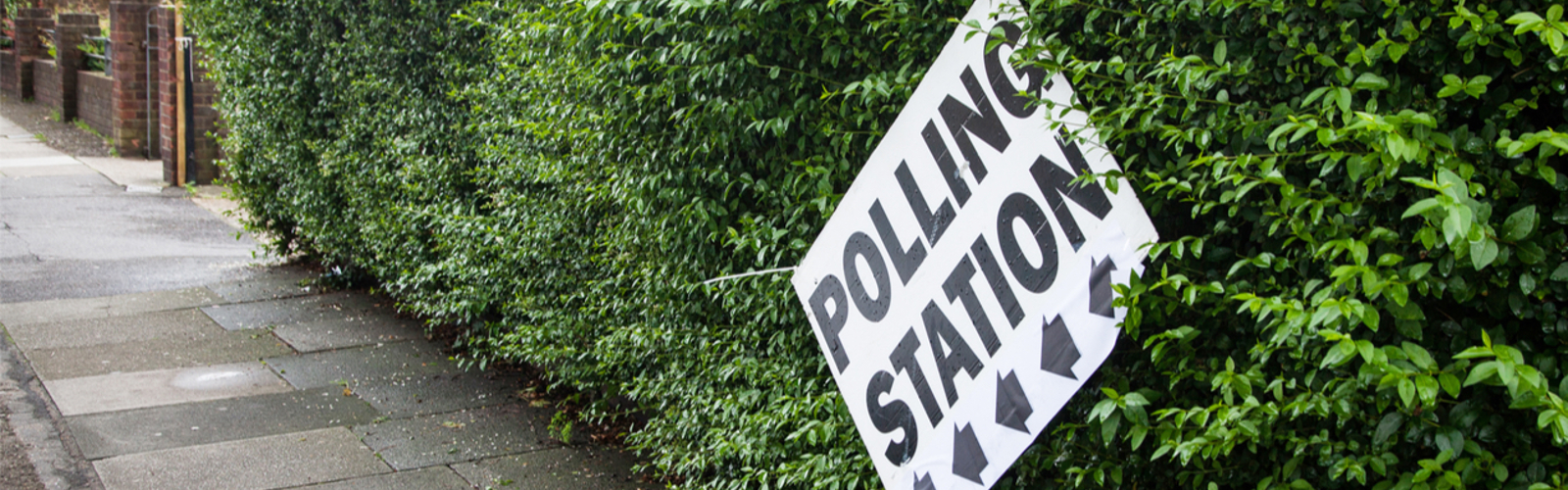 UK polling station sign, wonky against a green hedge