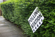 UK polling station sign, wonky against a green hedge