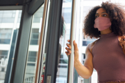 A woman in a mask pushes the handle of a door into an office building