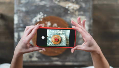 Cropped view of young adult food stylist using modern smartphone, making content for social media post.