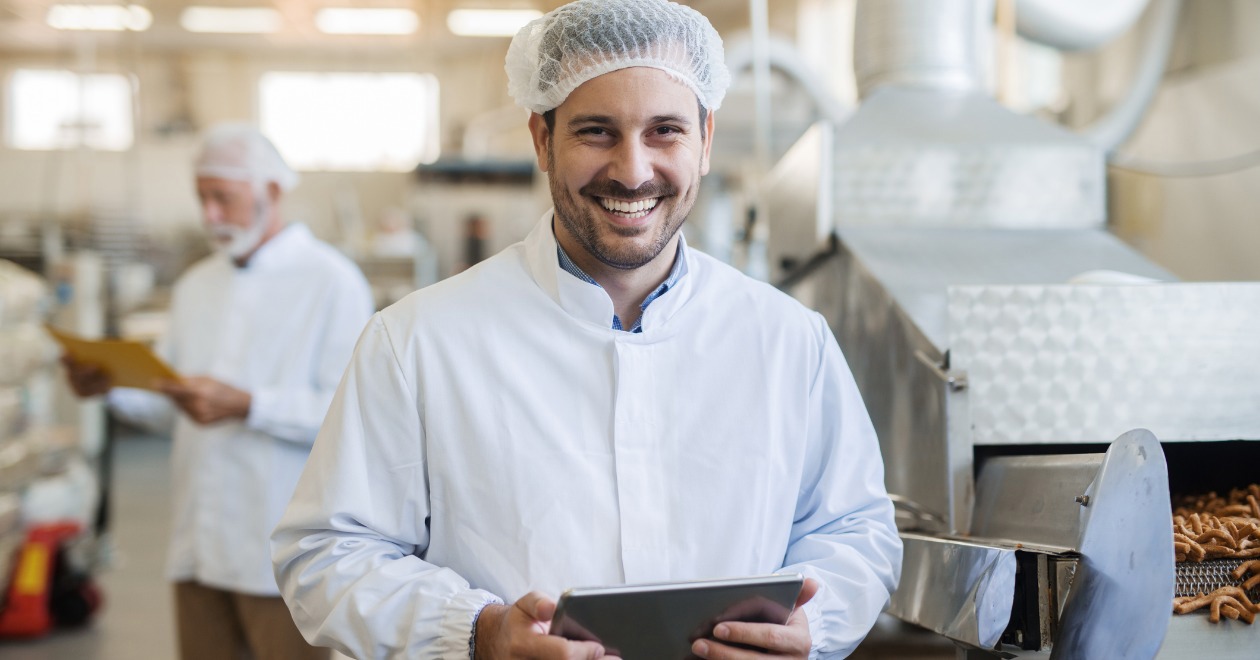 Male factory worker wearing white coat and hair net smiling