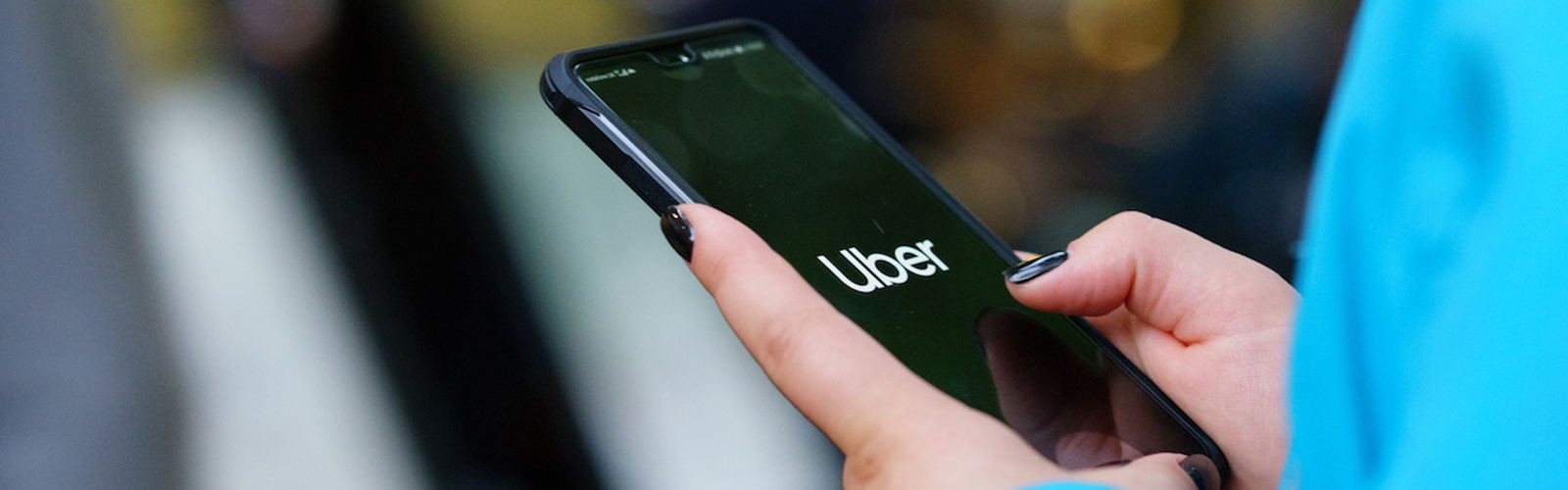 A woman holds a smartphone displaying the Uber logo