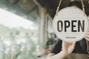 An 'open' sign in a shop window, with a person (face obscured by the sign) behind