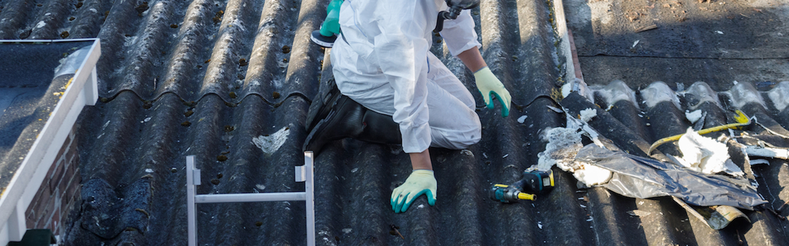 A person wearing protective clothing removing asbestos on a roof.