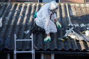 A person wearing protective clothing removing asbestos on a roof.