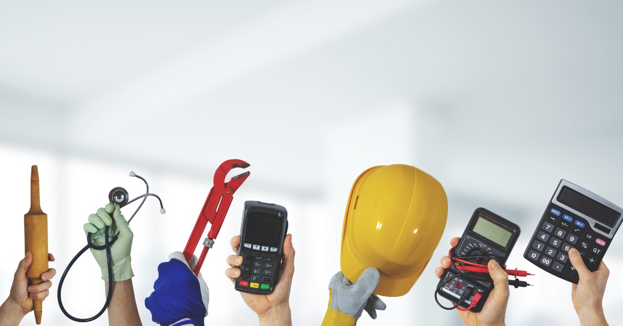 Hands holding up tools and equipment including a stethoscope, hard hat and a calculator