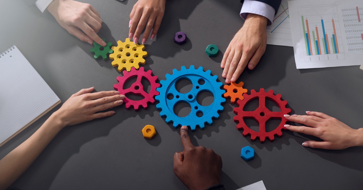 Six hands on a table turning colourful cogs