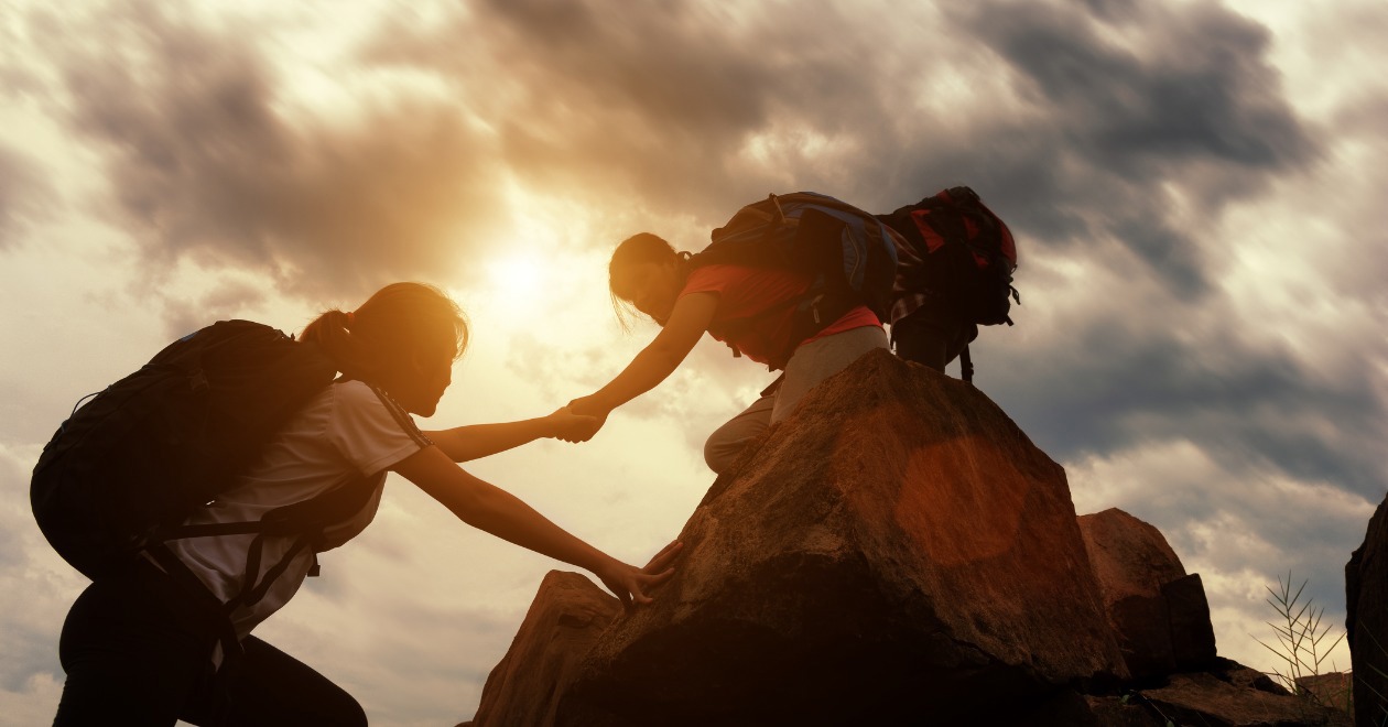 Two hikers helping each other up a hill at sunset.