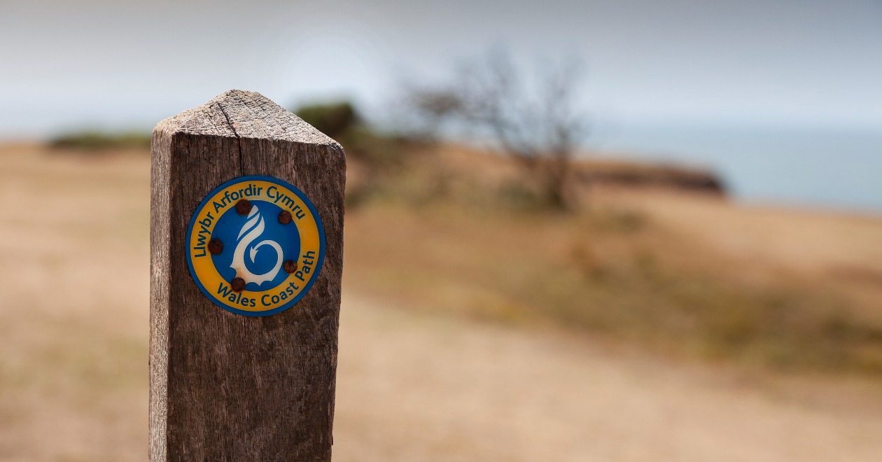 Wales Coast Path wooden sign and view of the sea