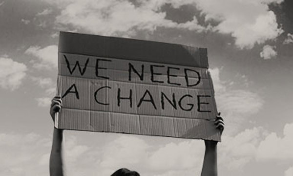 A person holding up a sign that says 'We need a change'