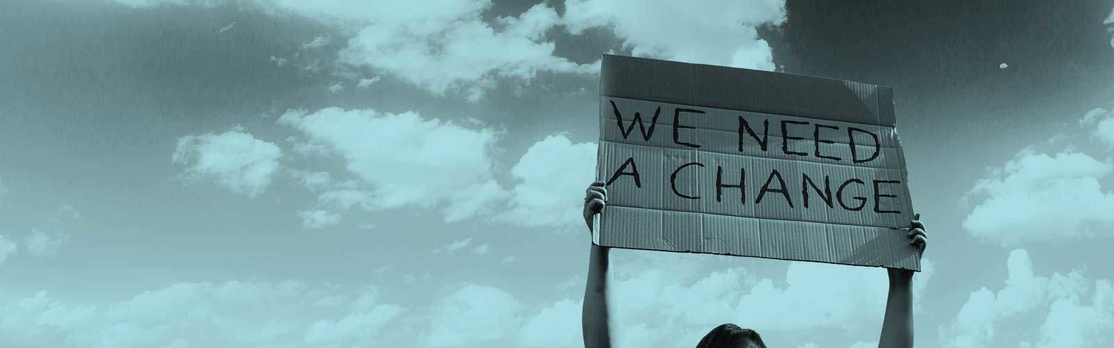 A person holding up a sign that says 'We need a change'