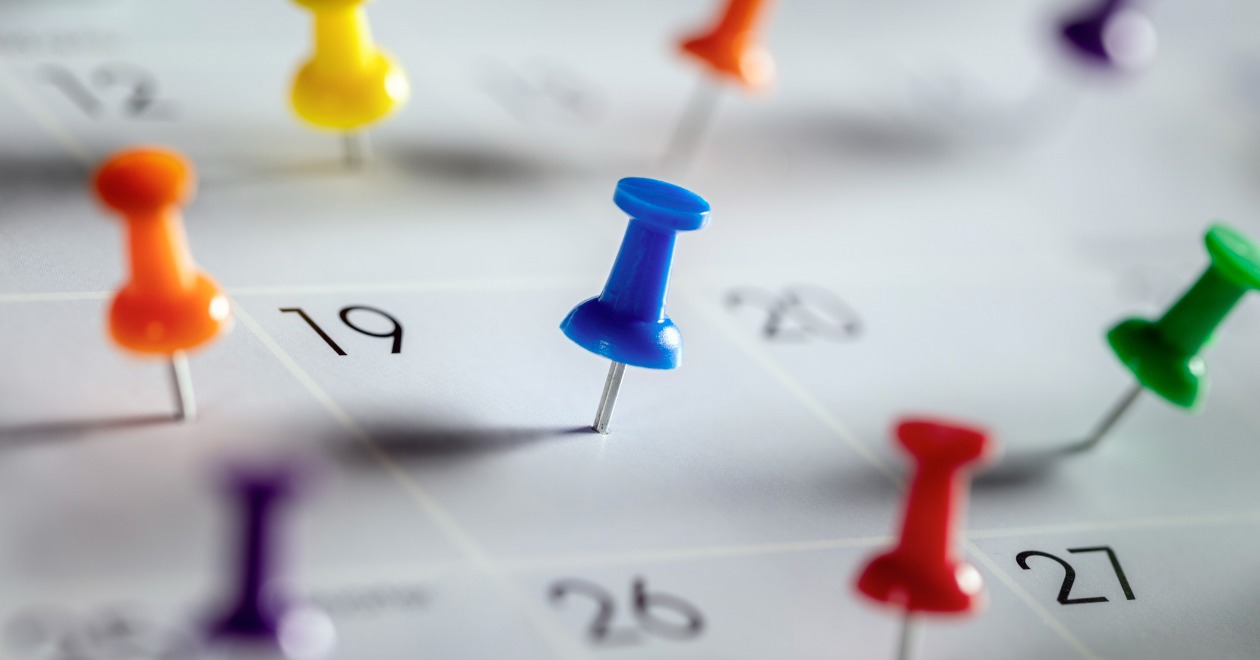 Colourful calendar appointment thumbtacks on various dates in a diary