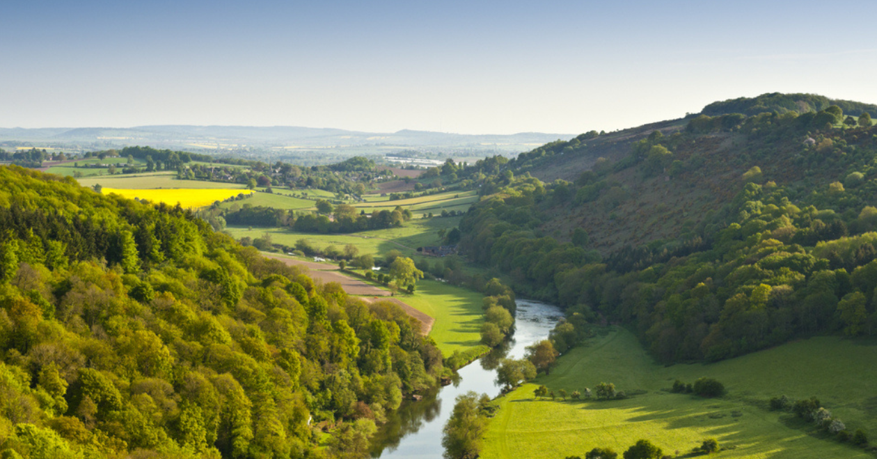 Meandering River Wye making its way through lush green rural farmland in the warm early sunlight.