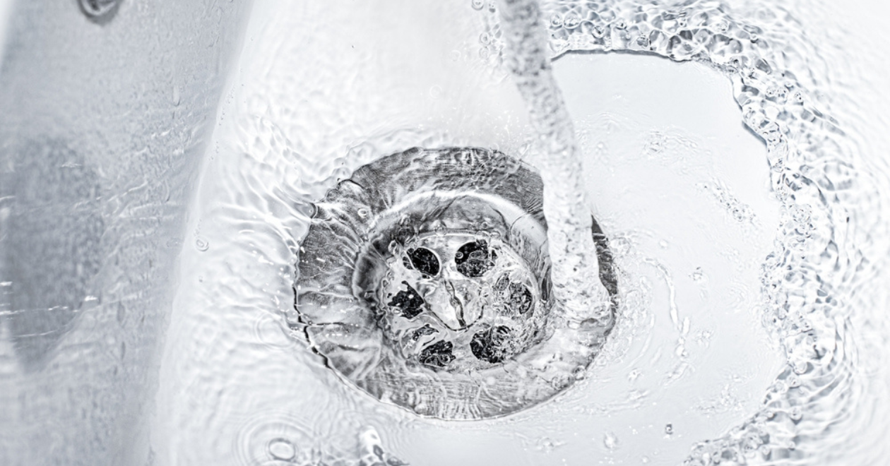 A jet of water flows into an open drain close-up