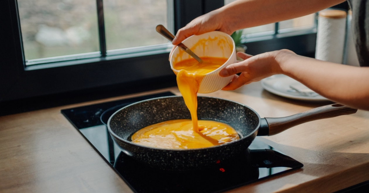 Someone pouring whisked eggs into frying pan